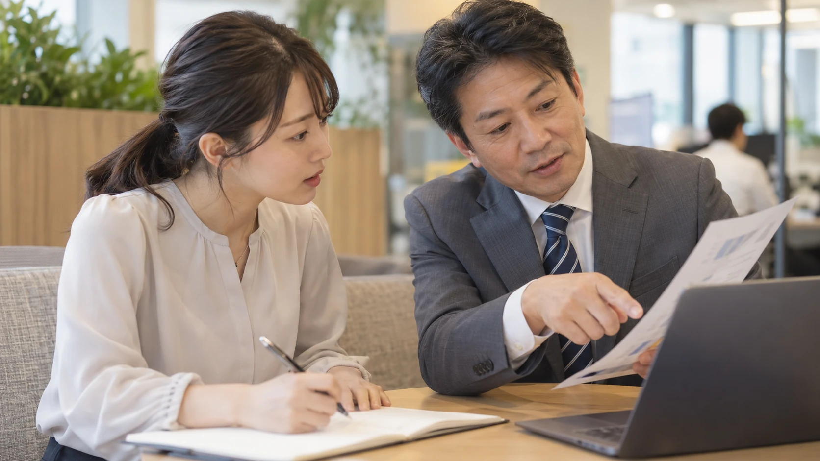 先輩の操作を見てノートを取り、新しい仕事の進め方を学ぶ情景